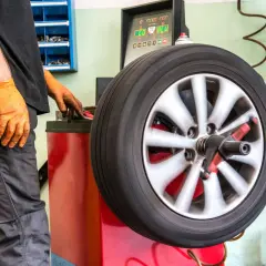 Taller mecánico realizando un equilibrado de ruedas. Un operario con guantes naranjas ajusta la máquina mientras la rueda gira.