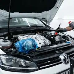 Hombre con guantes limpia el motor de un coche blanco con espuma y cepillo. Paso a paso, como limpiar el motor de un coche.