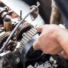 Mano ajustando las correas de un coche en el motor.