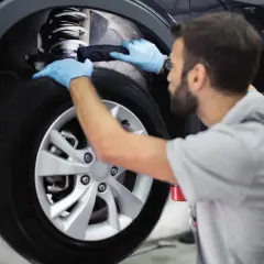 Mecánico con guantes azules revisa el amortiguador de un coche. Es importante recordar que hay que cambiar los 4 amortiguadores a la vez para un rendimiento óptimo.