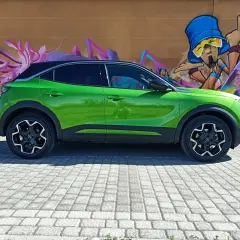 Coche verde eléctrico aparcado frente a un muro con grafitis coloridos. Podría tener problemas con su sistema mild hybrid.