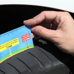 Una mano sostiene un medidor de profundidad de **neumático por dentro**, mostrando que la banda de rodadura está a 3 mm, cerca del límite legal de 1,6 mm.