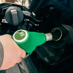 Mano con boquerel verde de gasolina sin plomo 95, repostando un coche negro.