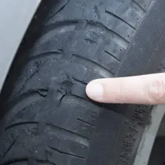 Dedo señala el desgaste de ruedas delanteras por el interior, mostrando daños severos en el caucho.
