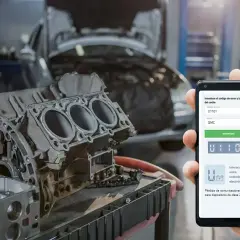 Mecánico revisa código de error U1101 en su móvil, junto a un motor de Mitsubishi.