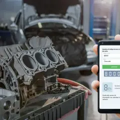 Mecánico revisa código de error OBD P0000 en su teléfono, mostrando un motor de Chevrolet en taller.