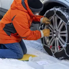 Persona con guantes ajusta la cadena del coche a la rueda cubierta de nieve.