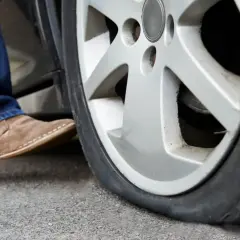 Un neumático pinchado, ¿qué es un runflat? Un pie con zapato de gamuza se acerca a la rueda desinflada.