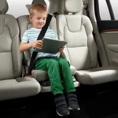 Niño sentado en asiento elevador integrado en el coche, entretenido con una tablet. Ideal para saber donde poner silla bebe coche.