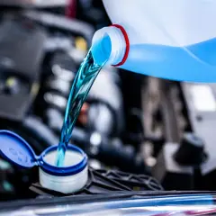 Líquido azul brillante se vierte de una botella a un depósito del coche. Es hora de decidir qué anticongelante usar para proteger tu motor.