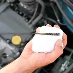 Mano limpiando la varilla del nivel de aceite en el motor. El aceite está entre las marcas de mínimo y máximo.
