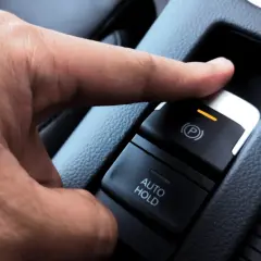 Dedo presionando el botón para desbloquear freno de mano eléctrico.
