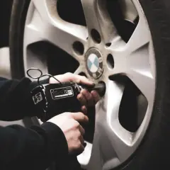 Mano usando una llave de impacto para cambiar ruedas delanteras por traseras en un coche BMW.