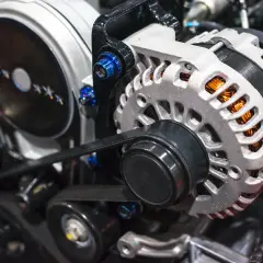 El alternador de un coche, con su polea y correa, genera electricidad. Se ve el motor y sus componentes.