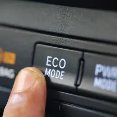 Dedo presionando el botón "ECO MODE" en un coche, optimizando el consumo de gasolina para viajes más eficientes.