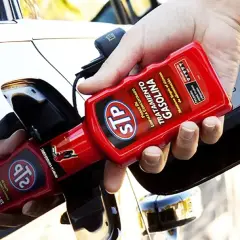Persona añadiendo aditivo STP a un coche de gasolina para su mantenimiento.