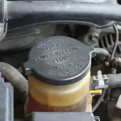 Depósito de líquido de dirección asistida. La tapa negra indica "POWER STEERING FLUID" y las marcas de nivel.