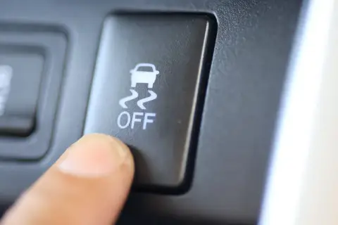 Dedo presionando el botón "OFF" del control de tracción, con el icono de un coche derrapando.