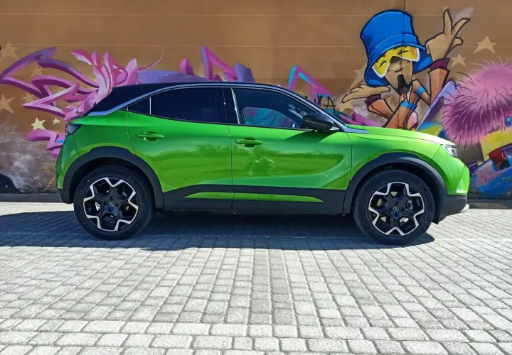 Coche verde eléctrico aparcado frente a un muro con grafitis coloridos. Podría tener problemas con su sistema mild hybrid.