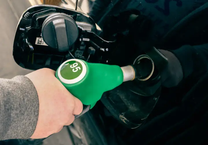 Mano con boquerel verde de gasolina sin plomo 95, repostando un coche negro.