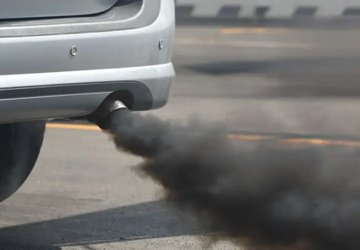 Humo negro al arrancar diésel, una nube densa sale del tubo de escape de un coche plateado.