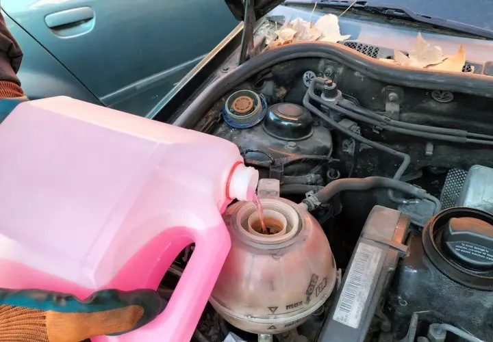 Persona con guantes vierte líquido refrigerante rosa en el depósito de expansión de un coche. Pregúntate cada cuanto se cambia el líquido refrigerante.