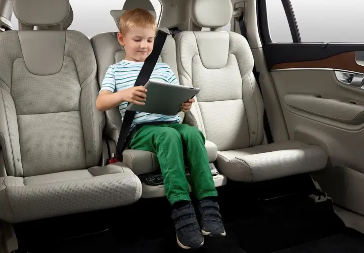 Niño sentado en asiento elevador integrado en el coche, entretenido con una tablet. Ideal para saber donde poner silla bebe coche.