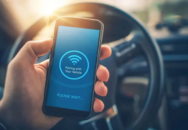 Mano sujetando un smartphone con pantalla que muestra "Pairing with Your Vehicle" y el icono de Bluetooth. Guía para saber como poner el bluetooth en el coche.