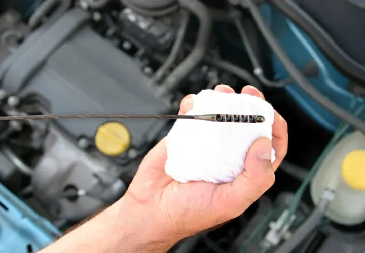 Mano limpiando la varilla del nivel de aceite en el motor. El aceite está entre las marcas de mínimo y máximo.