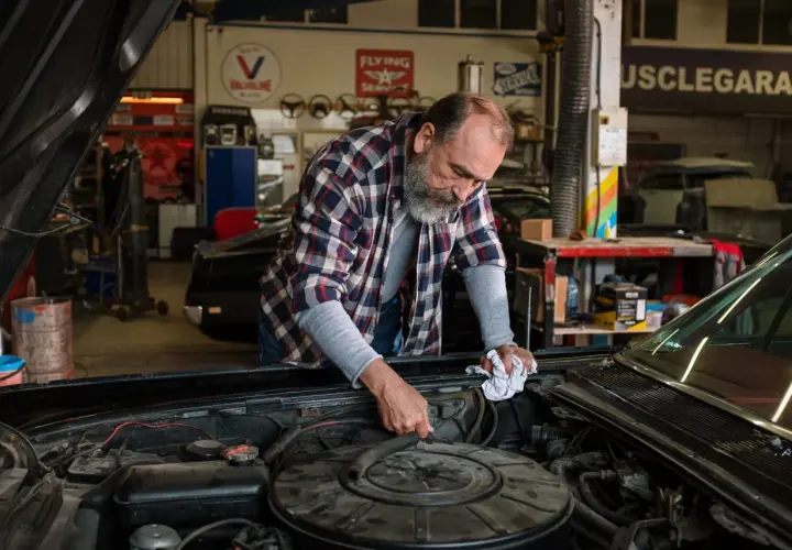 Mecánico revisa el motor de un coche clásico, buscando la causa por la que no salta el ventilador del coche.