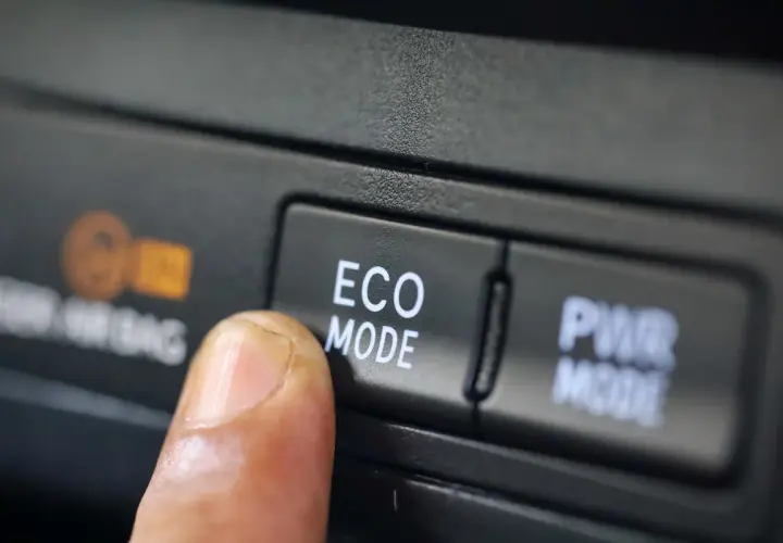 Dedo presionando el botón "ECO MODE" en un coche, optimizando el consumo de gasolina para viajes más eficientes.