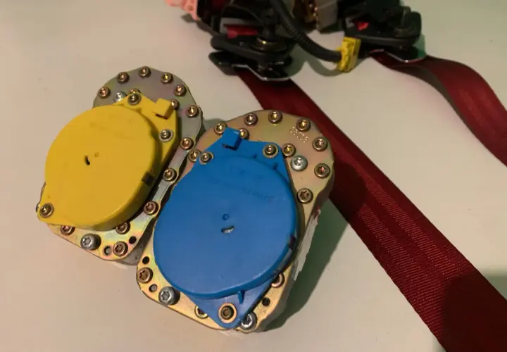 Mecanismo de cinturón de seguridad con carretes amarillo y azul, listo para reparar cinturón de seguridad deshilachado.