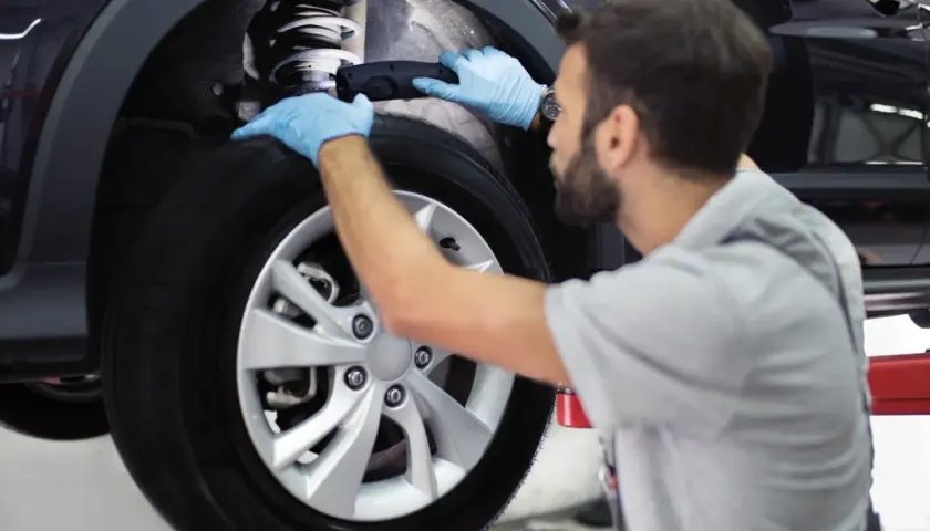 Mecánico con guantes azules revisa el amortiguador de un coche. Es importante recordar que hay que cambiar los 4 amortiguadores a la vez para un rendimiento óptimo.
