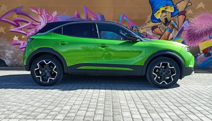 Coche verde eléctrico aparcado frente a un muro con grafitis coloridos. Podría tener problemas con su sistema mild hybrid.