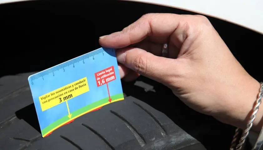 Una mano sostiene un medidor de profundidad de **neumático por dentro**, mostrando que la banda de rodadura está a 3 mm, cerca del límite legal de 1,6 mm.