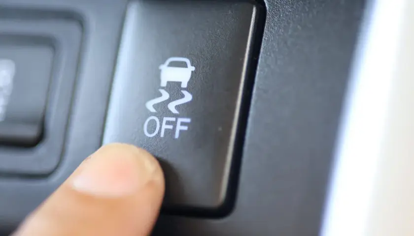 Dedo presionando el botón "OFF" del control de tracción, con el icono de un coche derrapando.