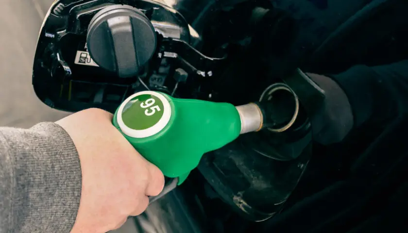 Mano con boquerel verde de gasolina sin plomo 95, repostando un coche negro.