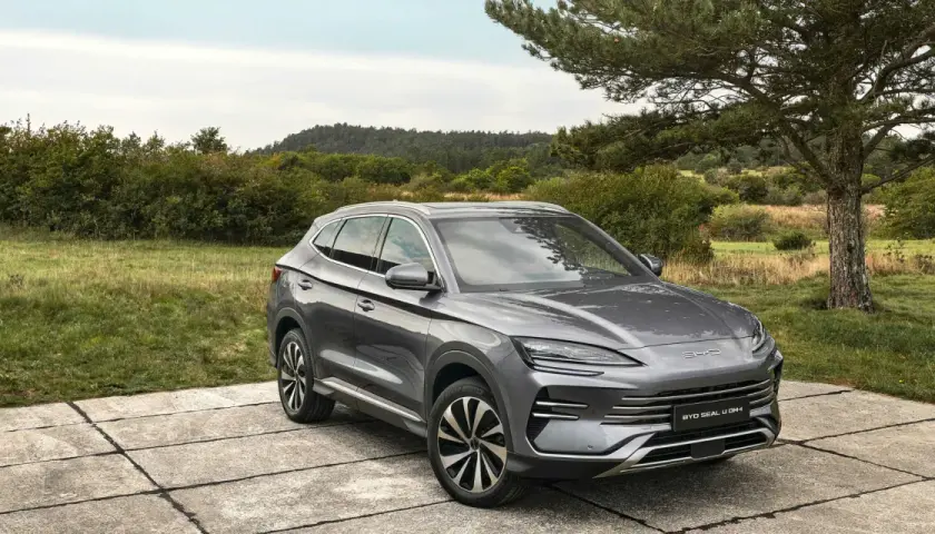 Un SUV gris moderno, uno de los coches híbridos autorrecargables, descansa sobre una plataforma de hormigón en un paisaje natural.