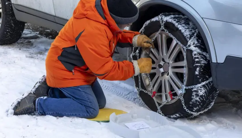 Persona con guantes ajusta la cadena del coche a la rueda cubierta de nieve.