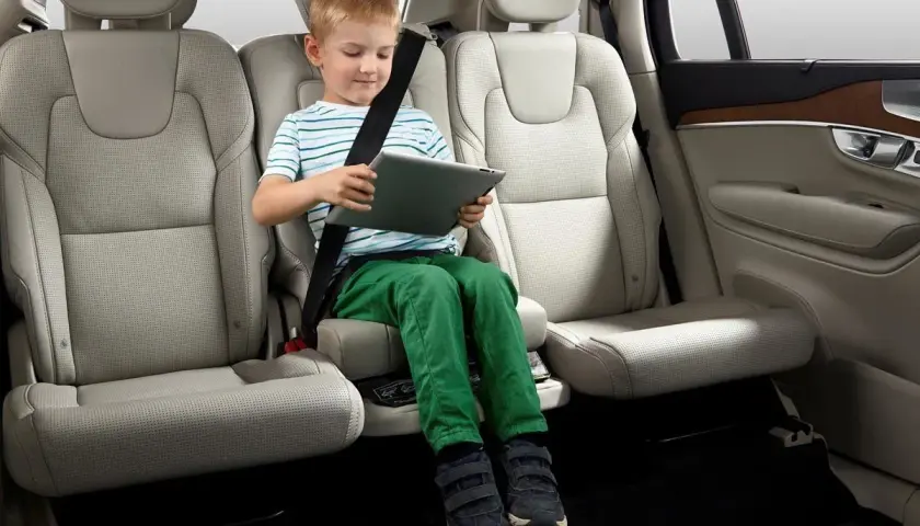 Niño sentado en asiento elevador integrado en el coche, entretenido con una tablet. Ideal para saber donde poner silla bebe coche.