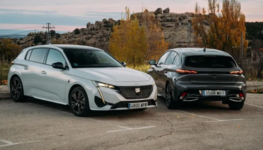 Dos Peugeot 308, uno blanco y otro gris oscuro, aparcados al aire libre. Los coches híbridos son diésel o gasolina, ofreciendo opciones eficientes.