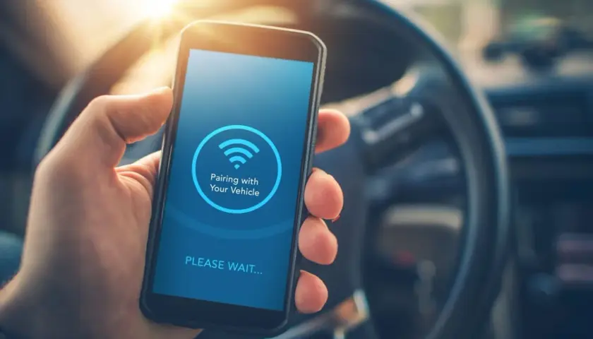 Mano sujetando un smartphone con pantalla que muestra "Pairing with Your Vehicle" y el icono de Bluetooth. Guía para saber como poner el bluetooth en el coche.
