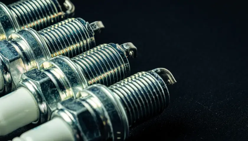 Cuatro bujías de encendido metálicas con rosca y aislante blanco, listas para dar vida a un motor. Los diesel llevan bujías, ¡y estas son las protagonistas!