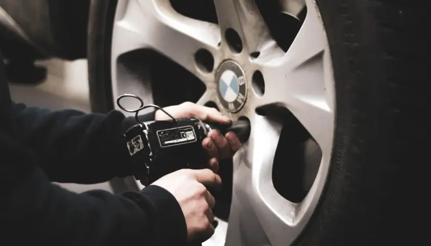 Mano usando una llave de impacto para cambiar ruedas delanteras por traseras en un coche BMW.