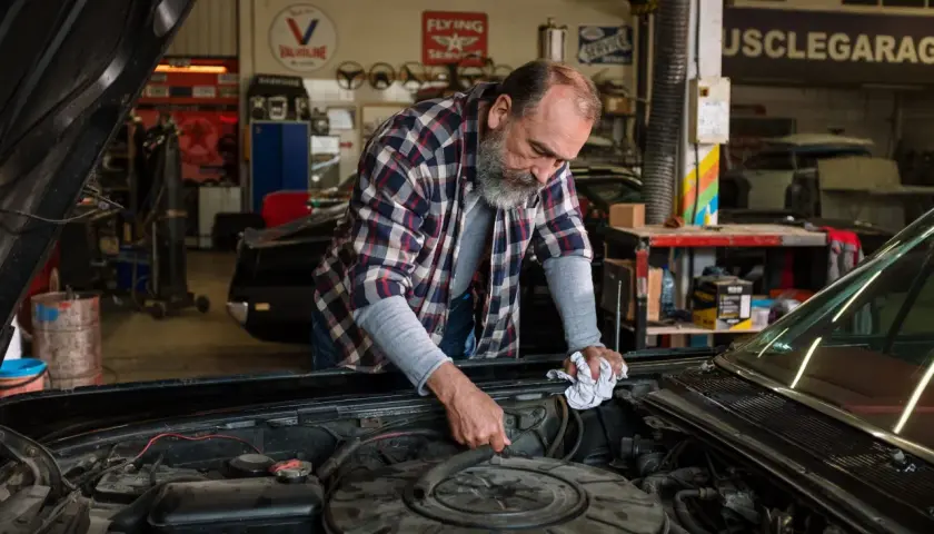 Mecánico revisa el motor de un coche clásico, buscando la causa por la que no salta el ventilador del coche.