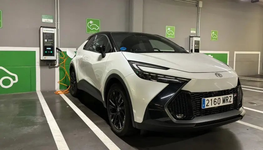 Coche híbrido blanco cargando en un parking. Las opiniones sobre este coche híbrido son muy positivas.