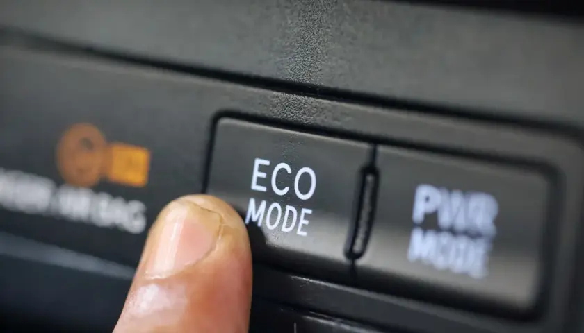 Dedo presionando el botón "ECO MODE" en un coche, optimizando el consumo de gasolina para viajes más eficientes.
