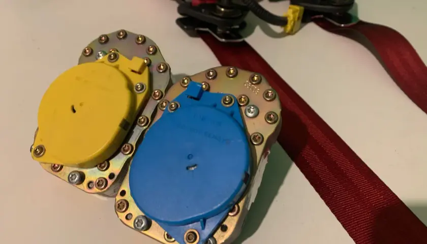 Mecanismo de cinturón de seguridad con carretes amarillo y azul, listo para reparar cinturón de seguridad deshilachado.