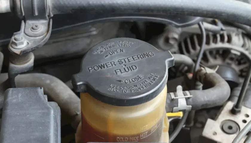 Depósito de líquido de dirección asistida. La tapa negra indica "POWER STEERING FLUID" y las marcas de nivel.