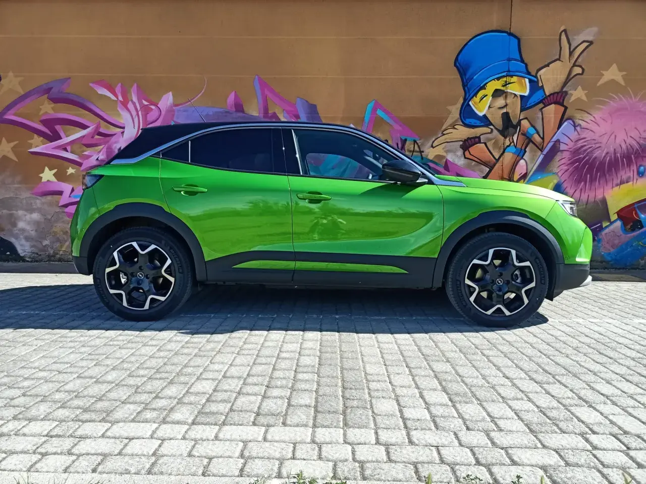 Coche verde eléctrico aparcado frente a un muro con grafitis coloridos. Podría tener problemas con su sistema mild hybrid.